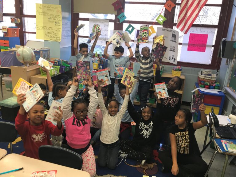 Elementary school students in a classroom excitedly hold up their new Book Trust books.